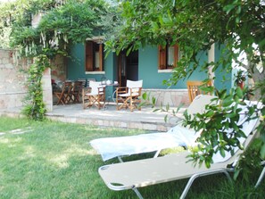 A patio area with outdoor furniture, a stone wall, and a green building with wooden shutters.
