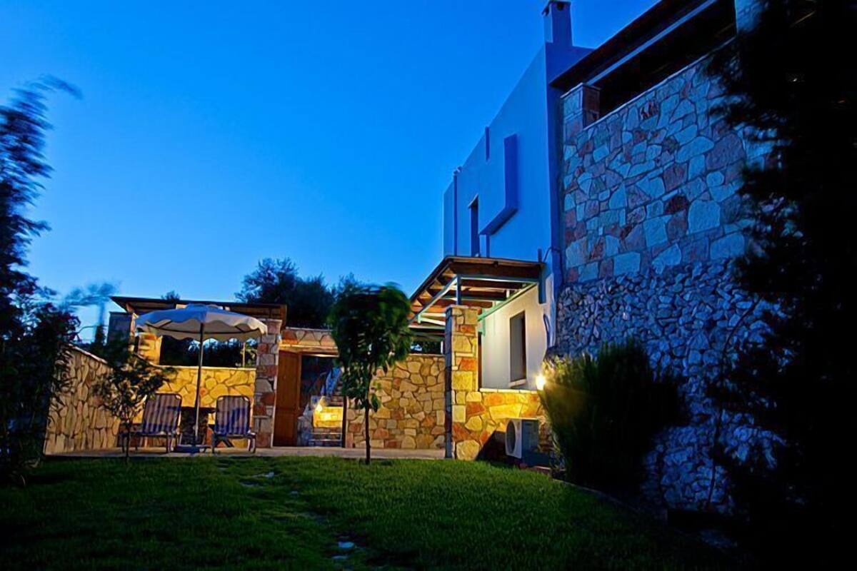 A modern house with a stone facade, a patio with chairs, and a covered seating area.