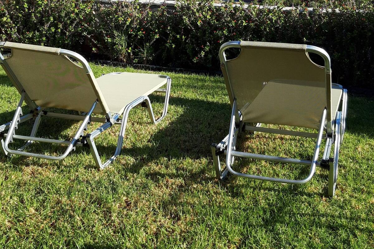 Two metal-framed lounge chairs with canvas seats on a grassy lawn, overlooking a coastal view with buildings in the distance.