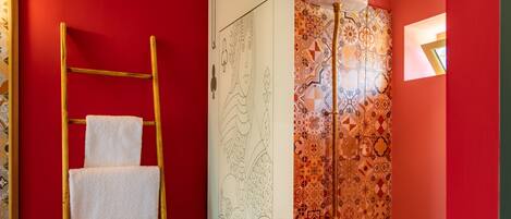 Un baño con pared roja, una escalera de madera con una toalla blanca, una cortina de ducha estampada y un inodoro de madera.