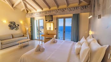 Un dormitorio amplio con una cama grande, un sofá, un escritorio y un balcón con vista al mar.