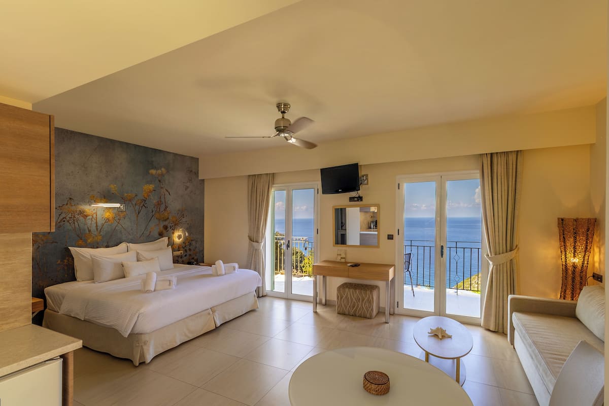 Een moderne hotelkamer met een groot bed, een bureau, een balkon met uitzicht op zee en een plafondventilator.