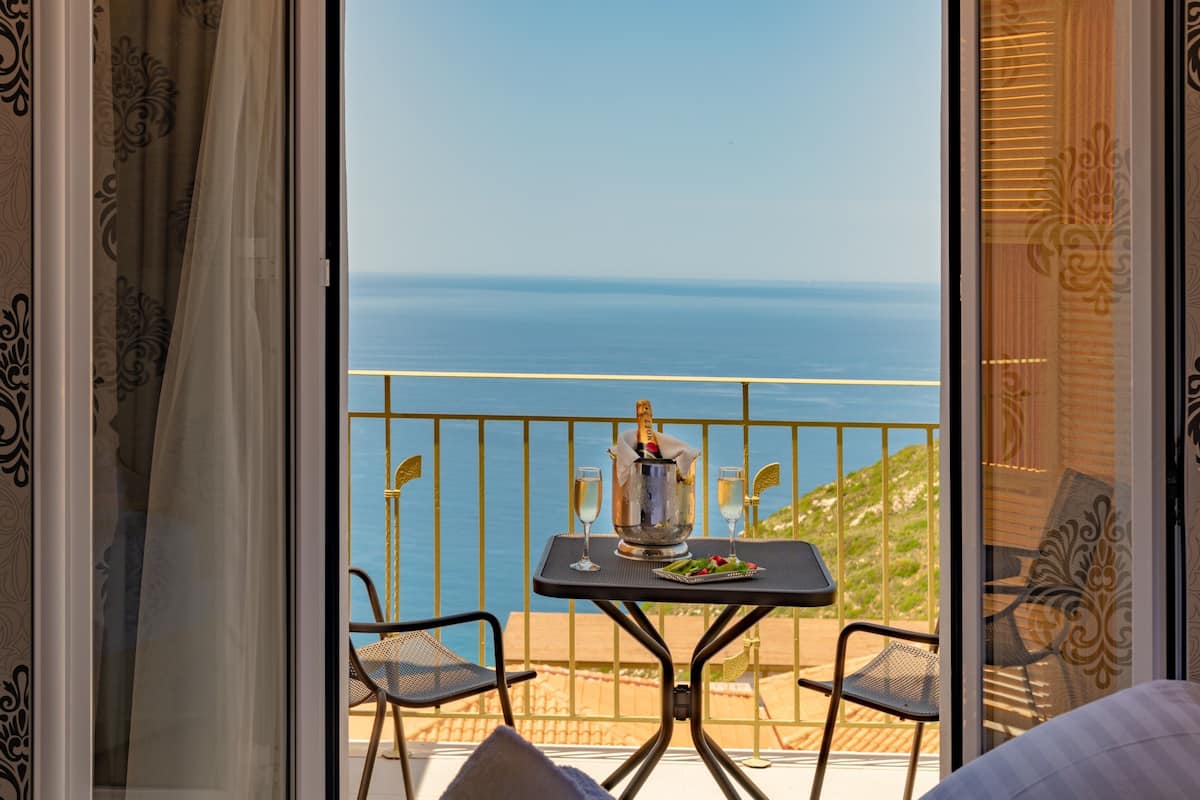 Een balkon met een tafel gedekt voor twee personen, een fles champagne en twee glazen. Vanuit het balkon is er uitzicht op de kust.
