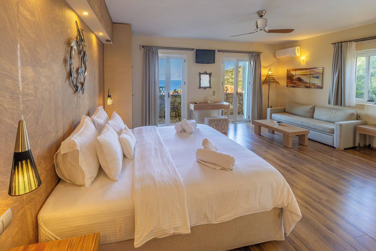 Een ruime slaapkamer met een groot bed, een slaapbank, een bureau en een balkon met uitzicht.