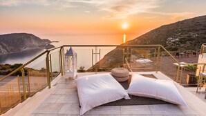 Eine Terrasse mit Blick auf den Sonnenuntergang über dem Meer, ausgestattet mit einer Couch, Kissen und einer Laterne.