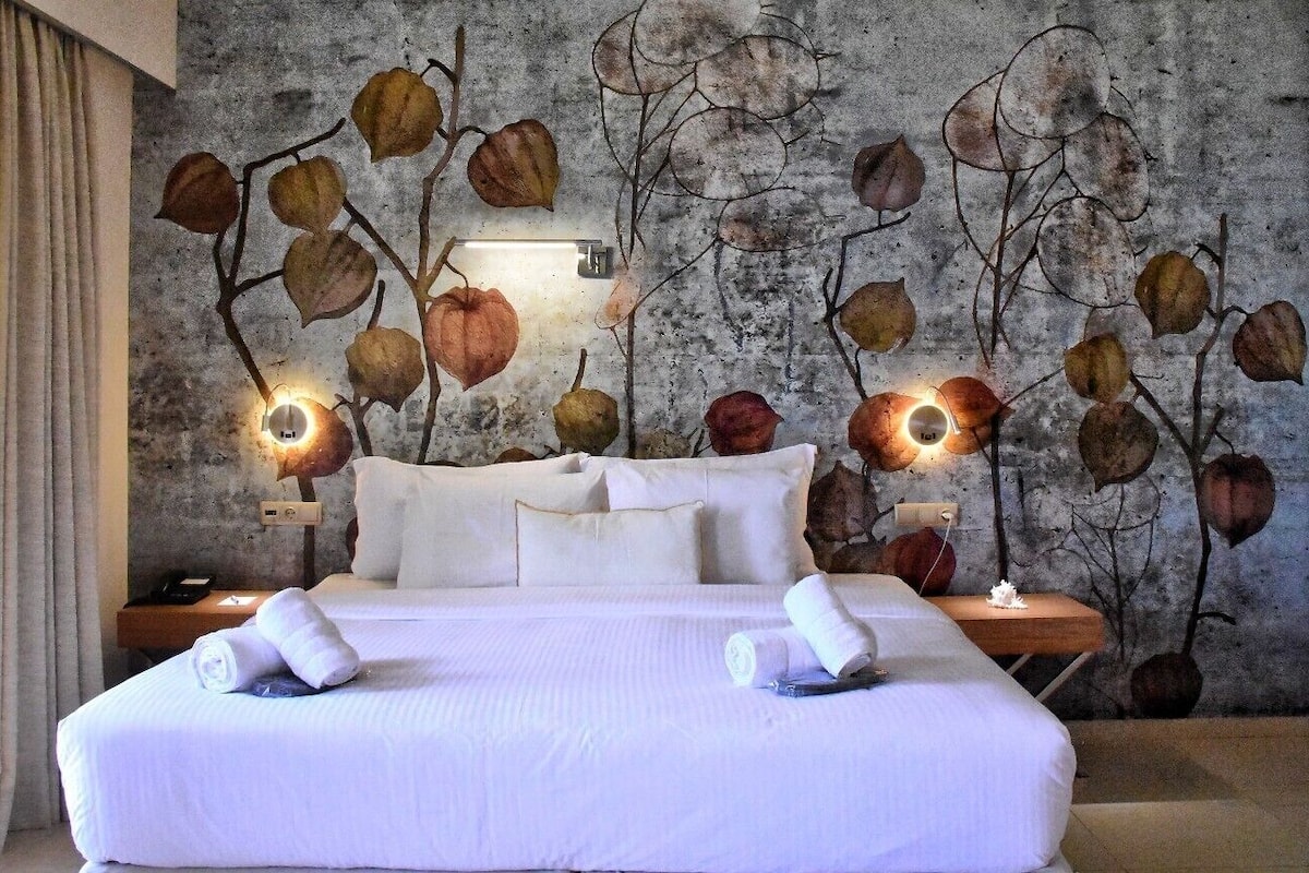Een hotelkamer met een groot bed, twee nachtkastjes en een muur met een bladmotief.