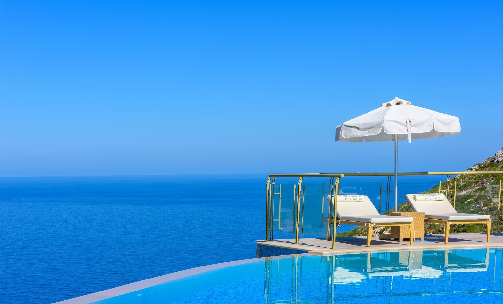 A poolside area with two lounge chairs and a white umbrella, overlooking the sea.