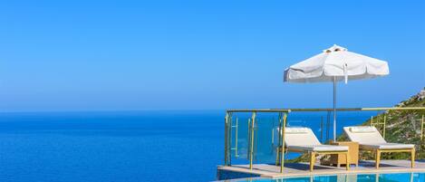 A poolside area with two lounge chairs and a white umbrella, overlooking the sea.