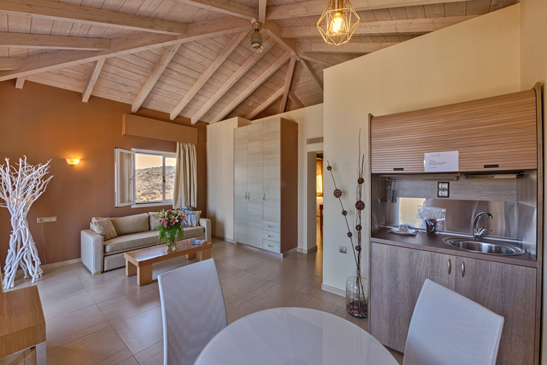 Ein modernes Interieur mit Essbereich, einer Couch, einer Küche mit Edelstahlgeräten und einem Ausblick durch ein Fenster.