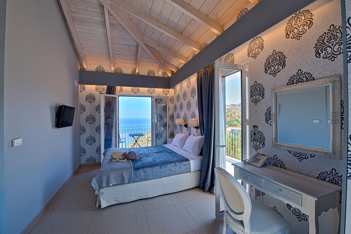 Een slaapkamer met een bed, een bureau en uitzicht op zee.