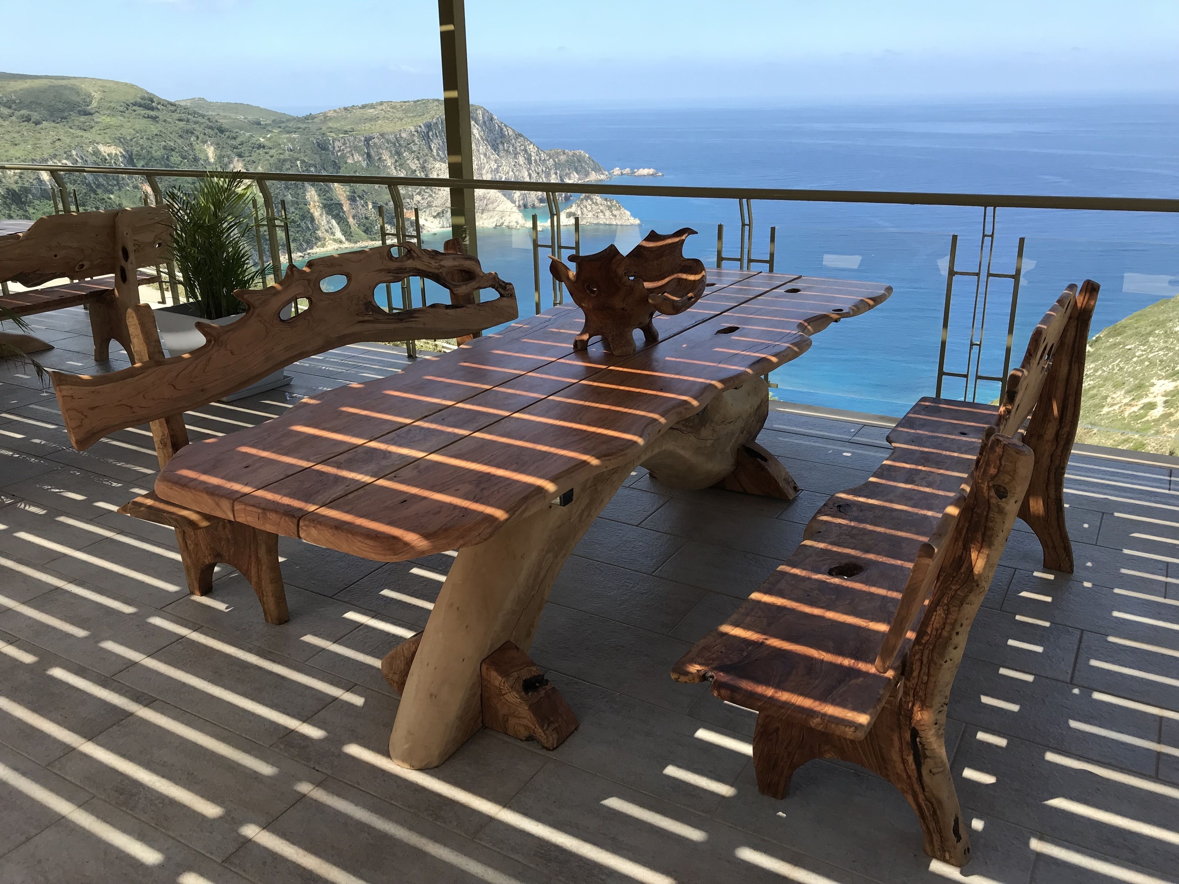 An outdoor seating area with wooden tables and benches, overlooking a coastal landscape.