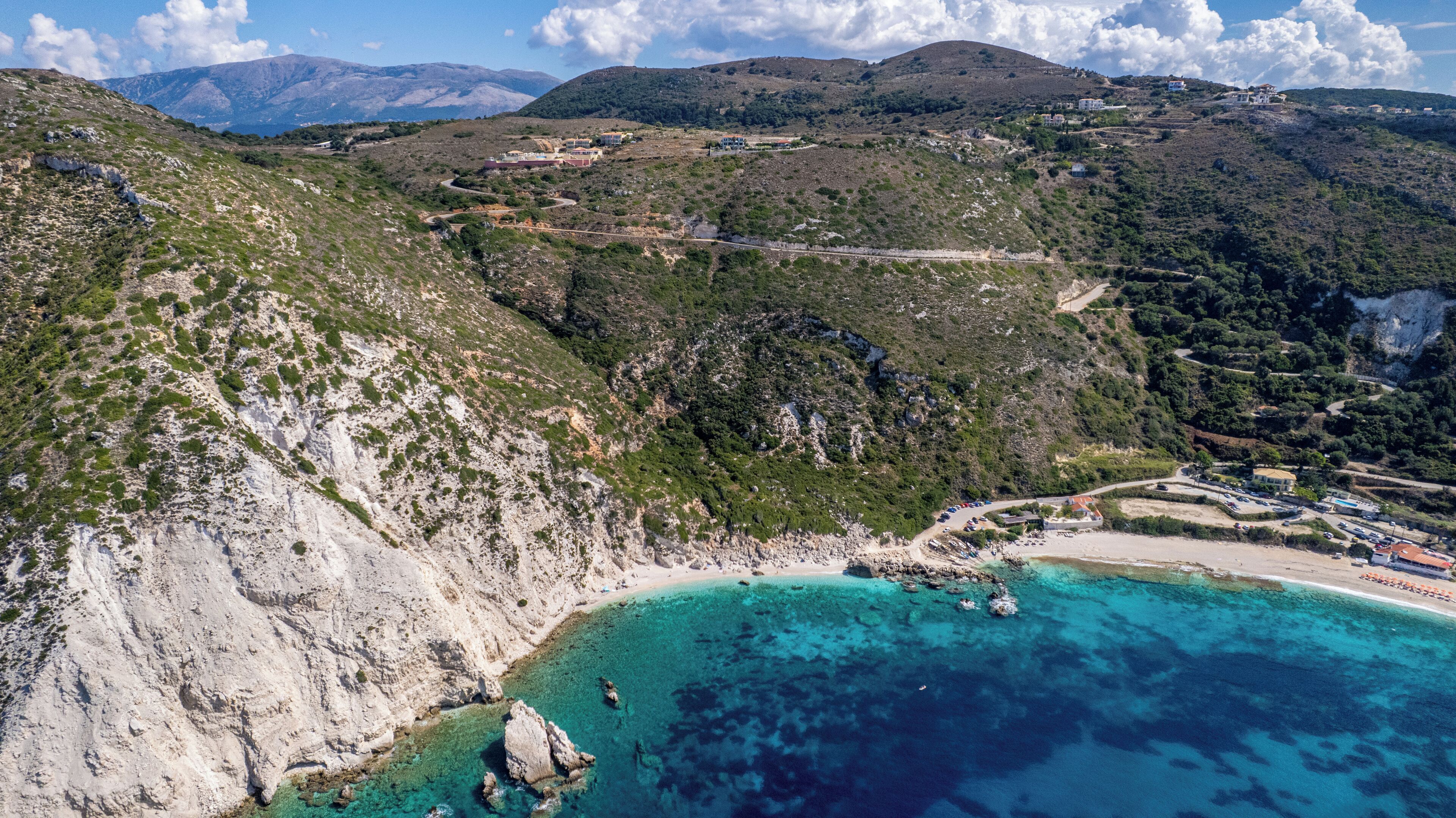 A coastal area with a beach, rocky cliffs, and a mountainous backdrop.