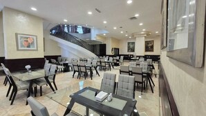 A spacious dining area with multiple tables and chairs, a staircase, and artwork on the walls. - Le Vendôme Hotel (Amman)