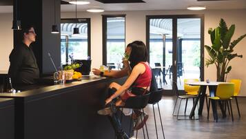 Zona de bar moderna con mostrador, taburetes y una gran planta en maceta.