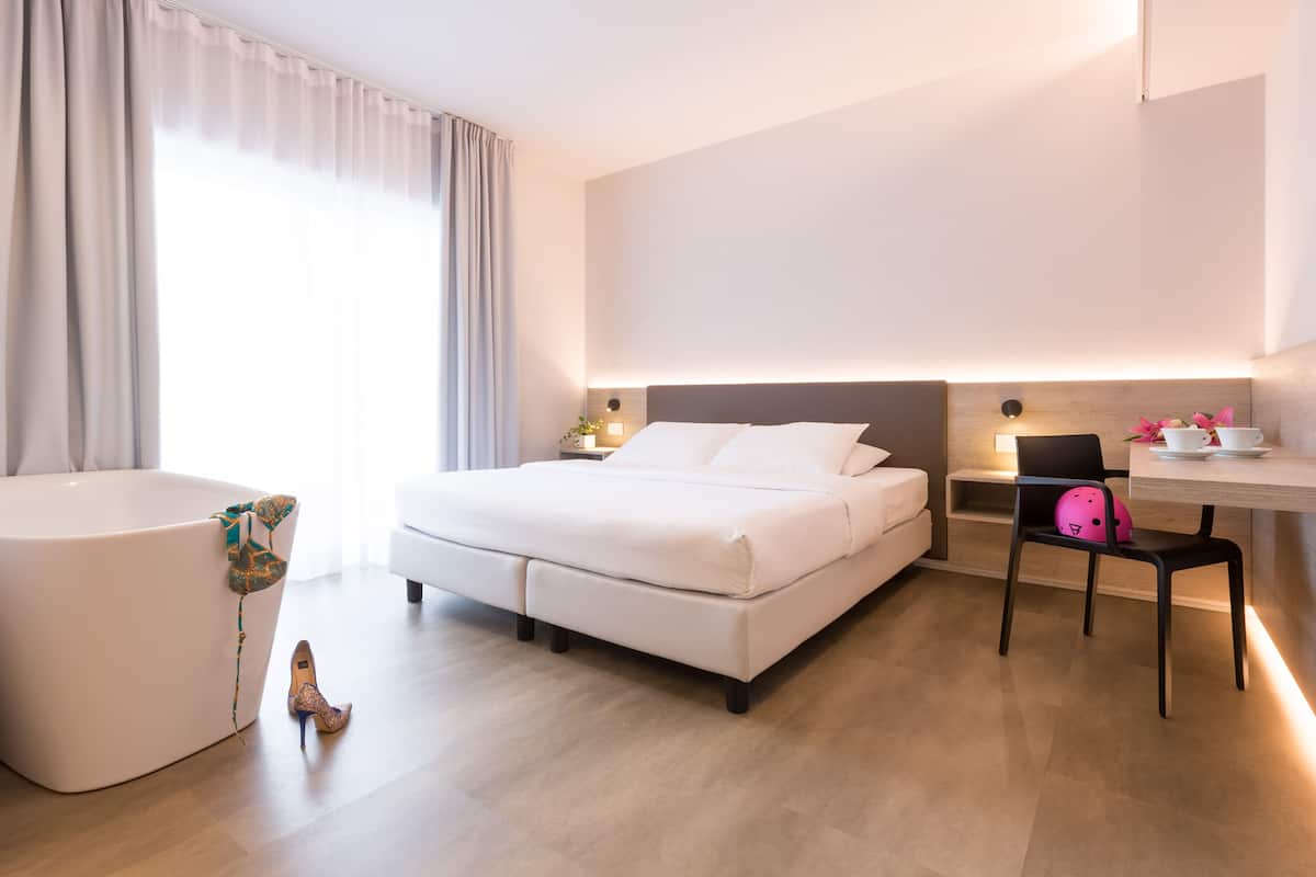 Moderni hotellihuone, jossa on suuri sänky, työpöytä, tuoli ja kylpyamme.