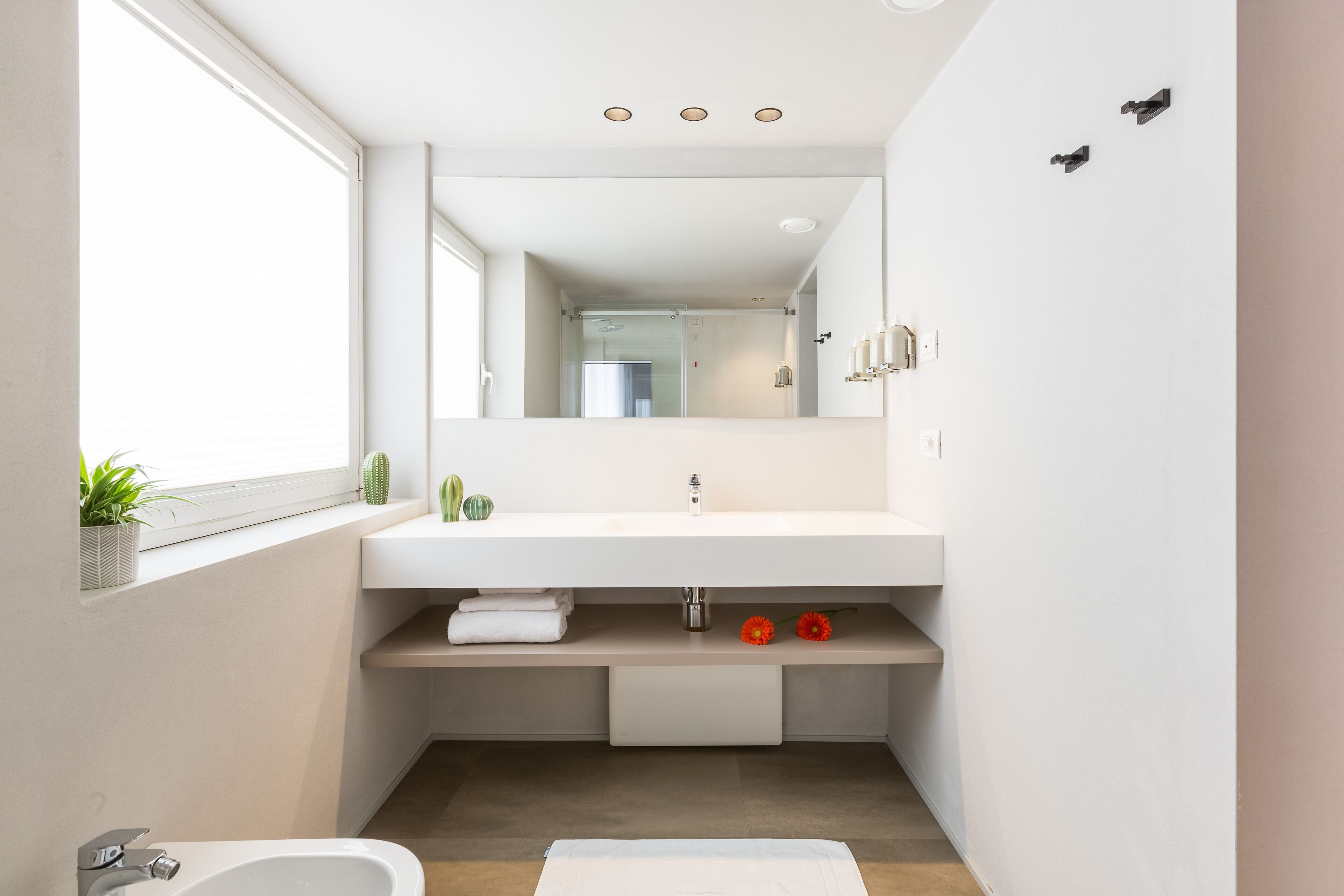 A modern bathroom with a white sink, a mirror, and a window.