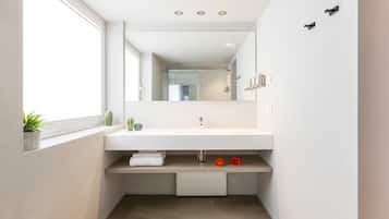 A modern bathroom with a white sink, a mirror, and a window.