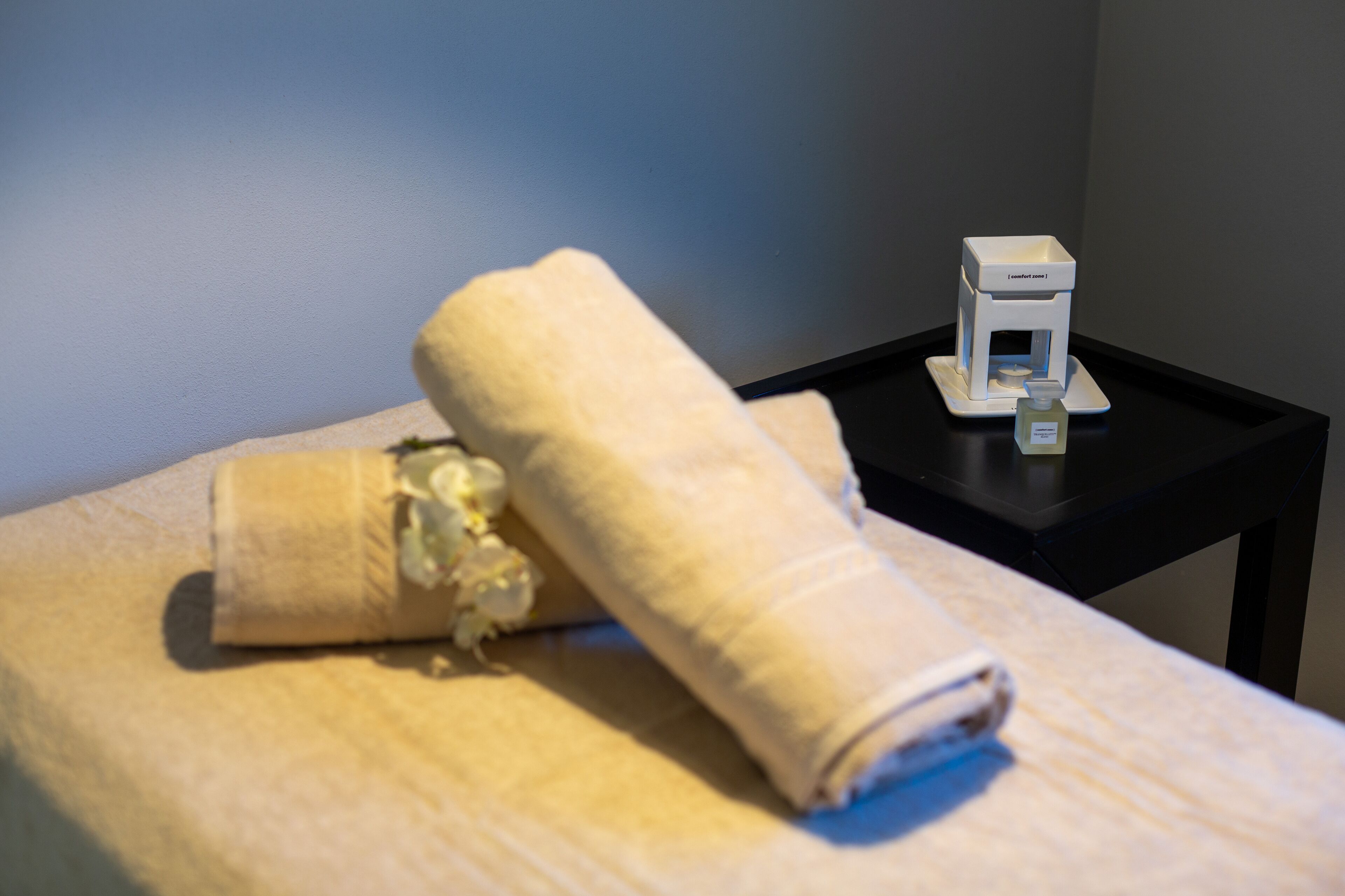 A neatly folded towel on a bed with a small white object on a black side table.