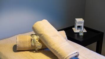 A neatly folded towel on a bed with a small white object on a black side table.