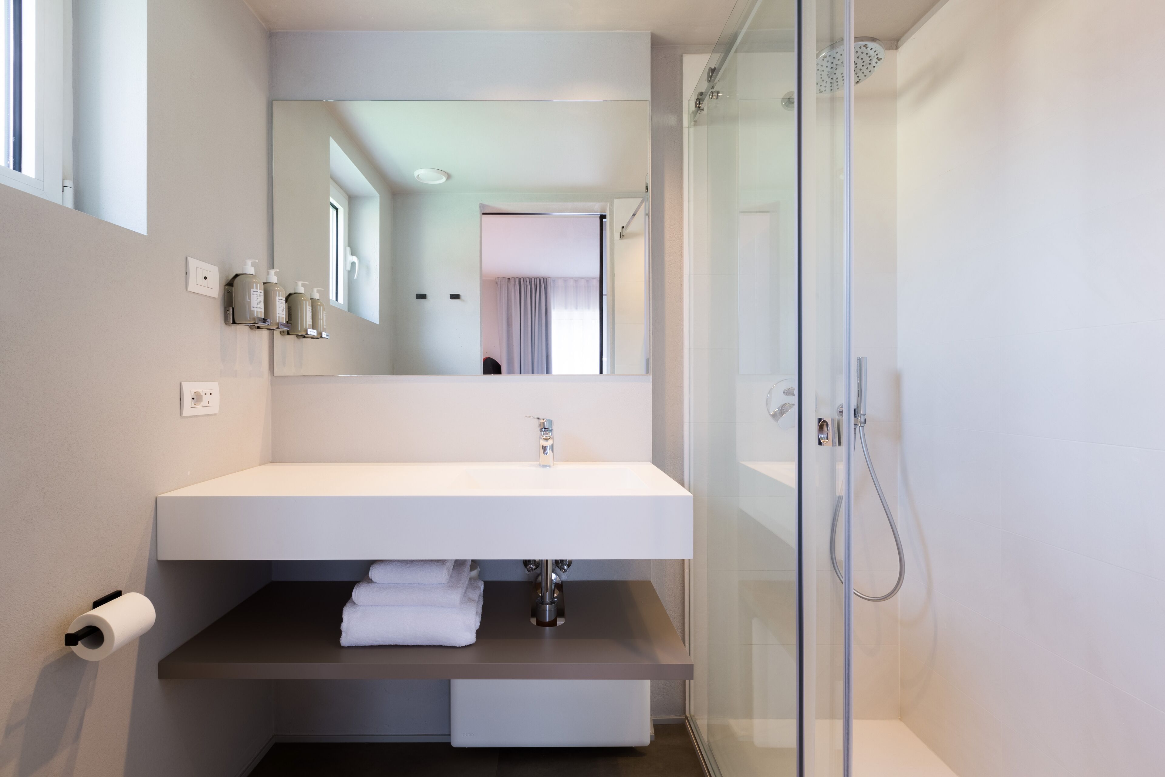 A modern bathroom with a white sink, mirror, and glass shower enclosure.