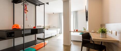 A modern hotel room with a bed, a desk with a chair, a shelf with a helmet, and a plant.