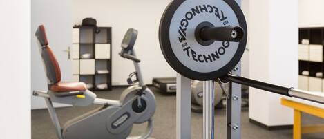 A weightlifting machine with a digital display, a bench, and a wall-mounted shelf with items.
