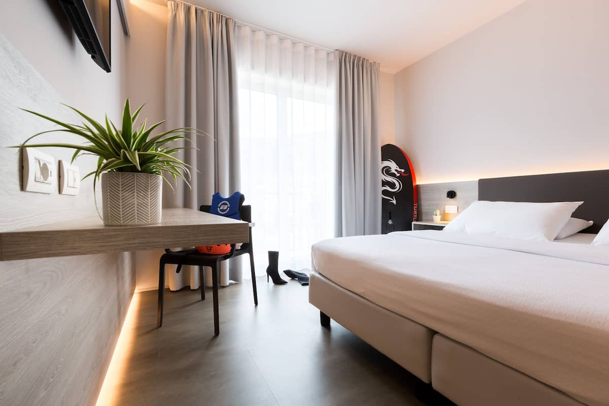 Moderni hotellihuone, jossa on sänky, työpöytä, tuoli, ruukkukasvi ja surffilauta.