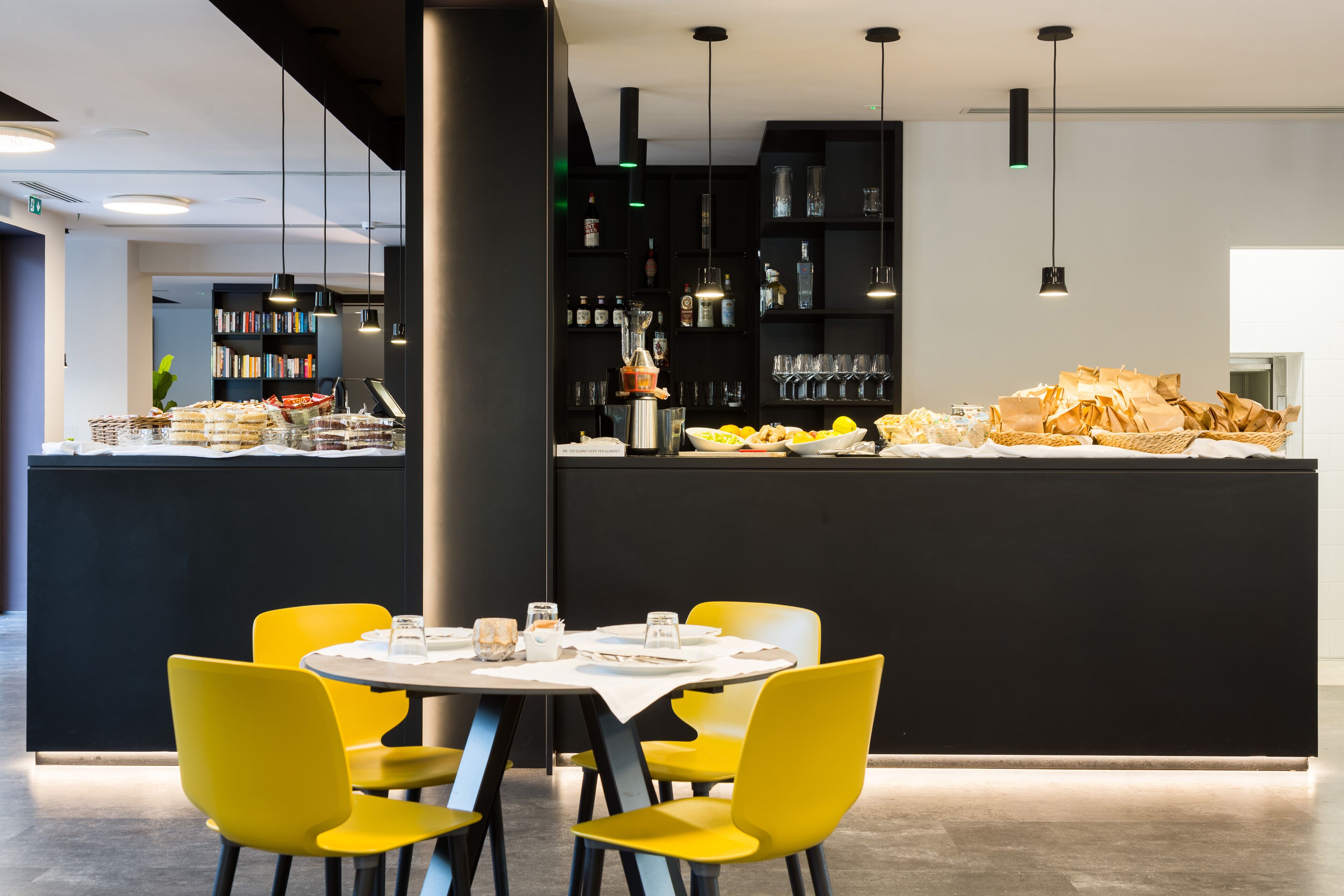Un comedor moderno con barra negra, sillas amarillas y mesa blanca.
