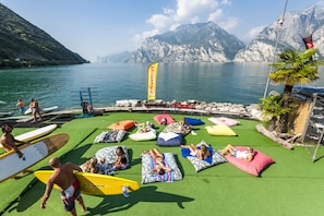 Un área junto a la piscina con césped artificial, sillas de descanso y vistas a un lago y montañas.