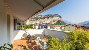 Eine Terrasse mit Tisch und Stühlen mit Blick auf eine gebirgige Landschaft, im Hintergrund sind Gebäude zu sehen.