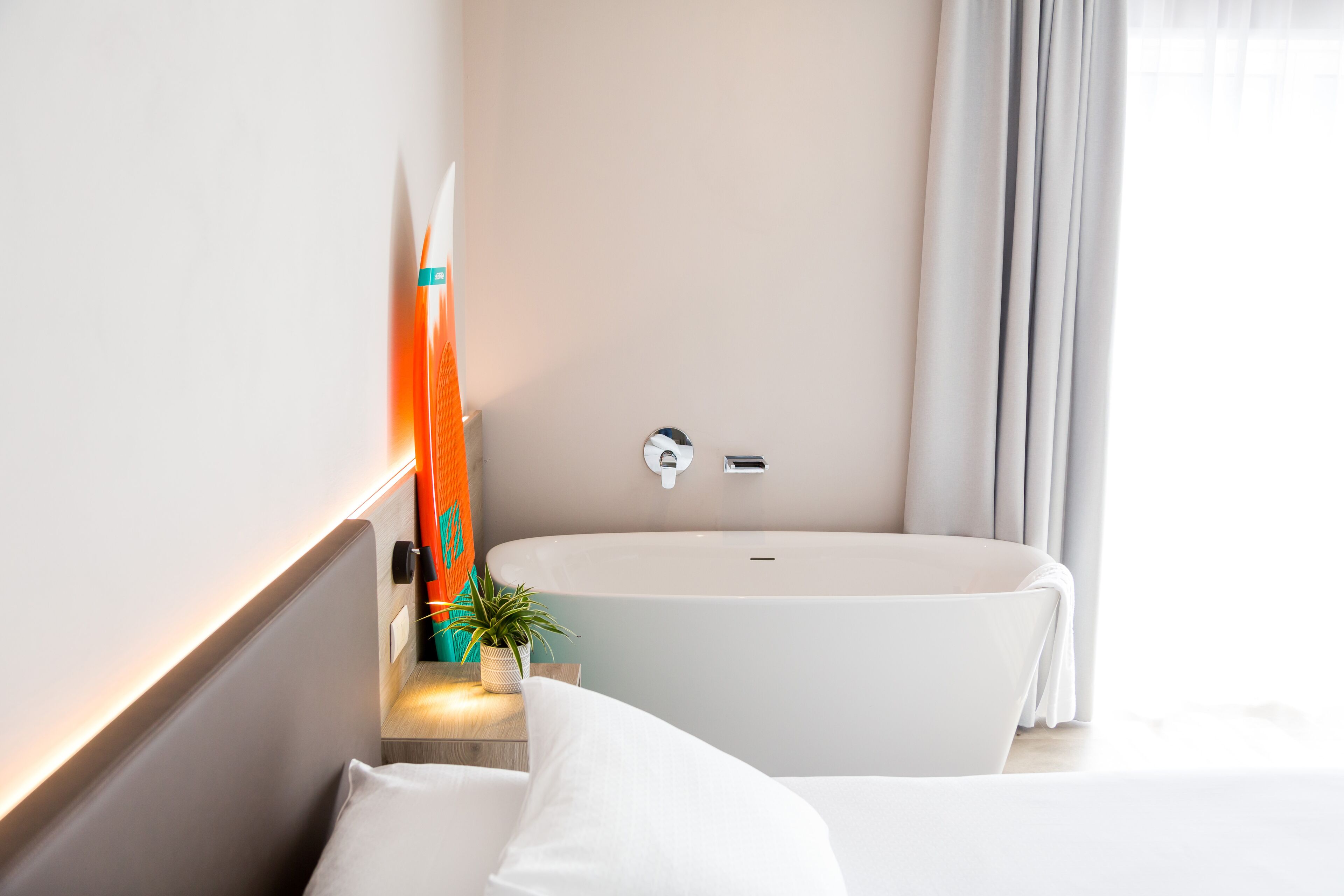 Un baño moderno con una bañera independiente, una pequeña planta en maceta y un perchero para toallas.