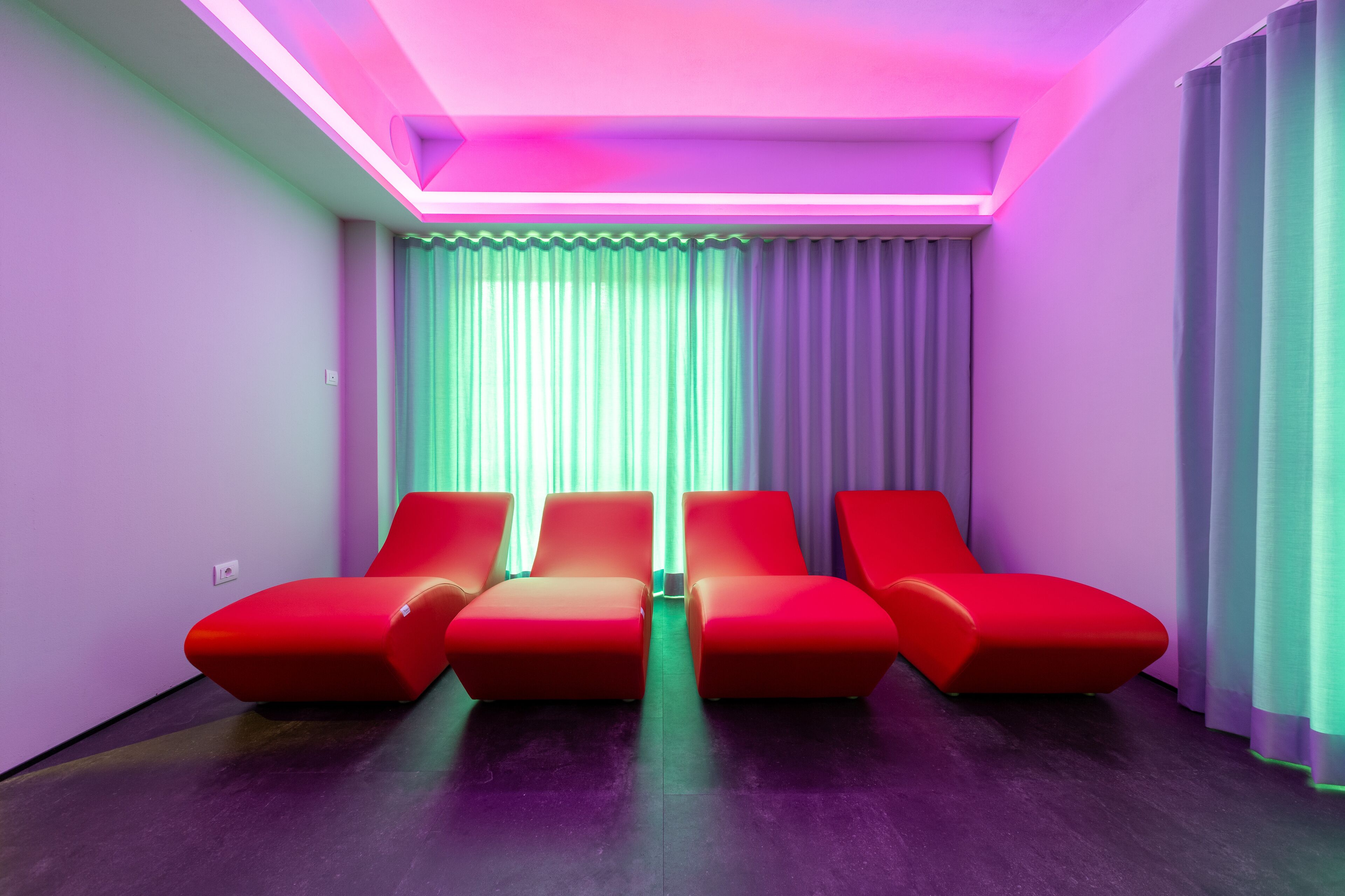 A room with a modern design, featuring a seating area with red chairs and a large window with curtains.