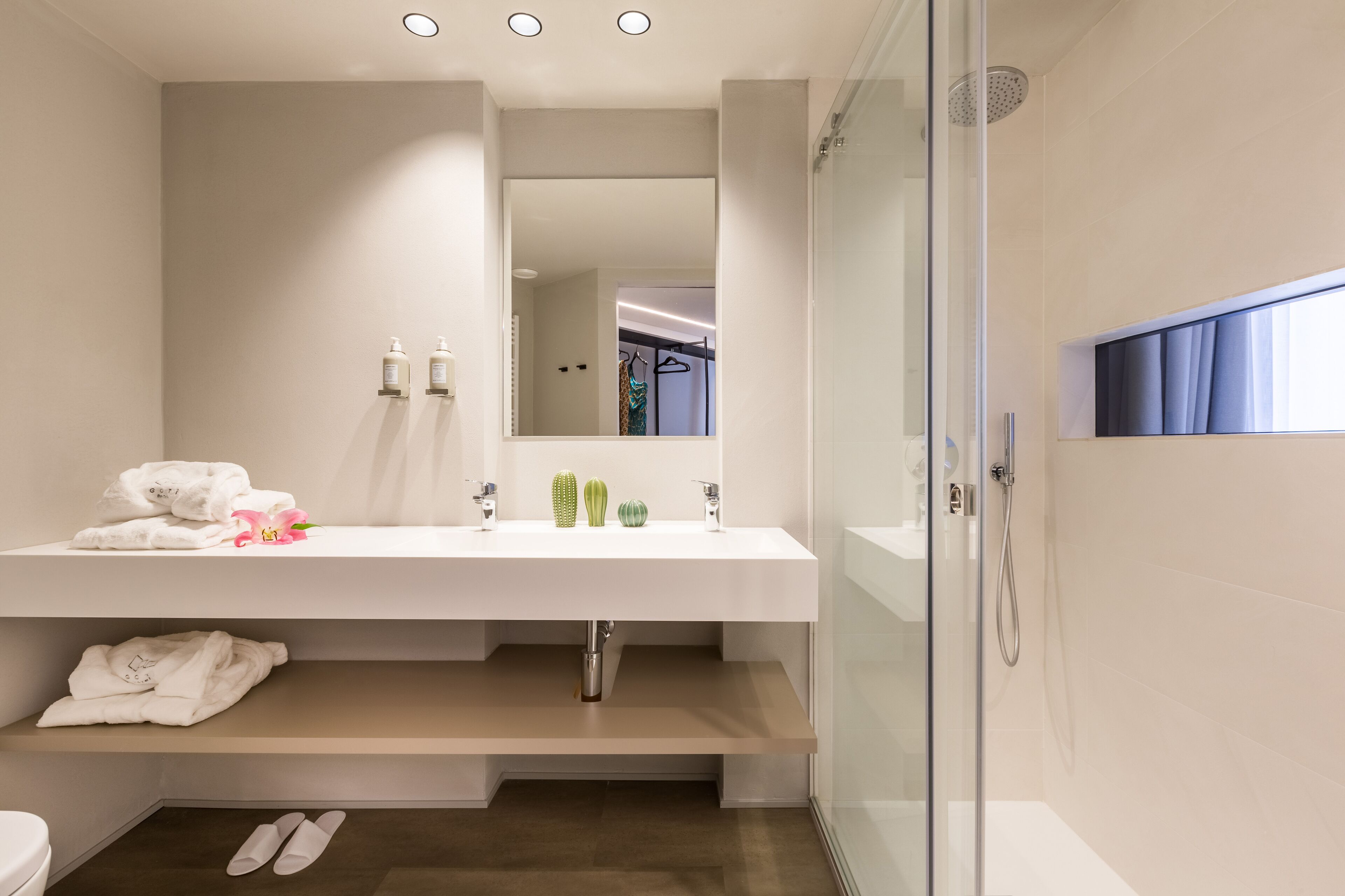 A modern bathroom with a white vanity, a glass shower enclosure, and a visible hallway in the mirror reflection.