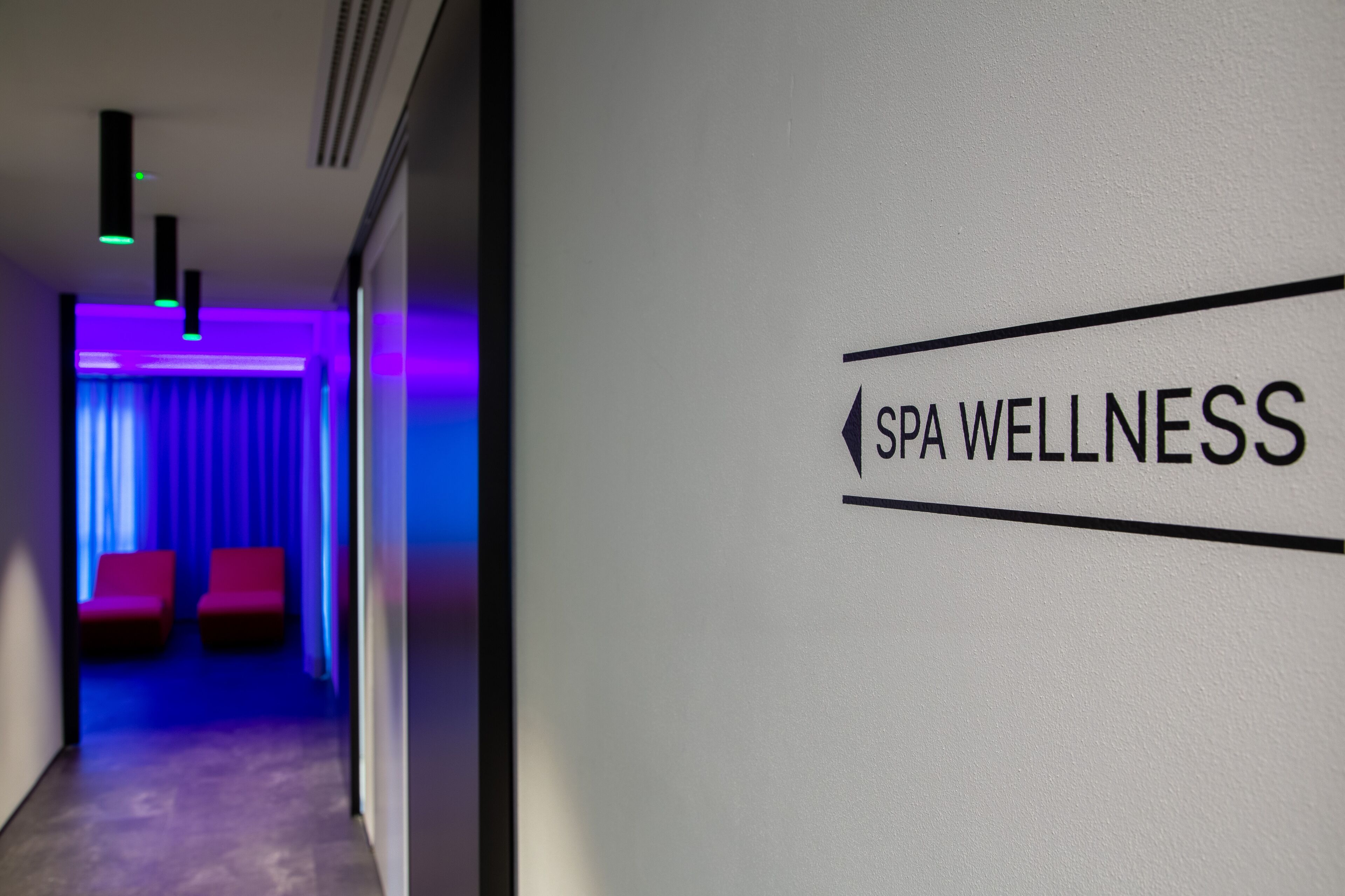 Un pasillo con un letrero que dice "SPA WELLNESS" y una habitación con asientos rojos e iluminación azul.