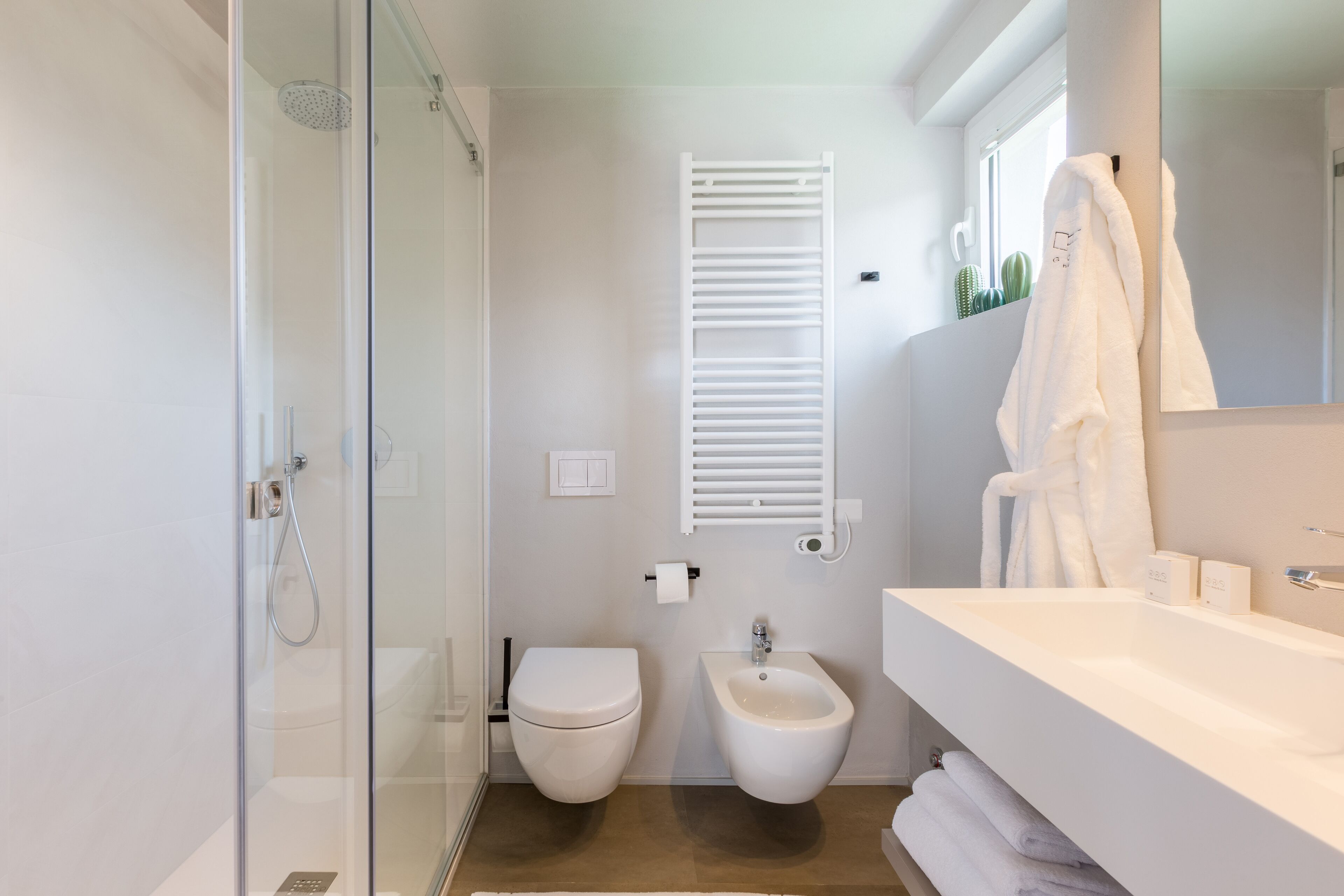 A modern bathroom with a glass shower enclosure, a white toilet, a bidet, and a large sink with a mirror.