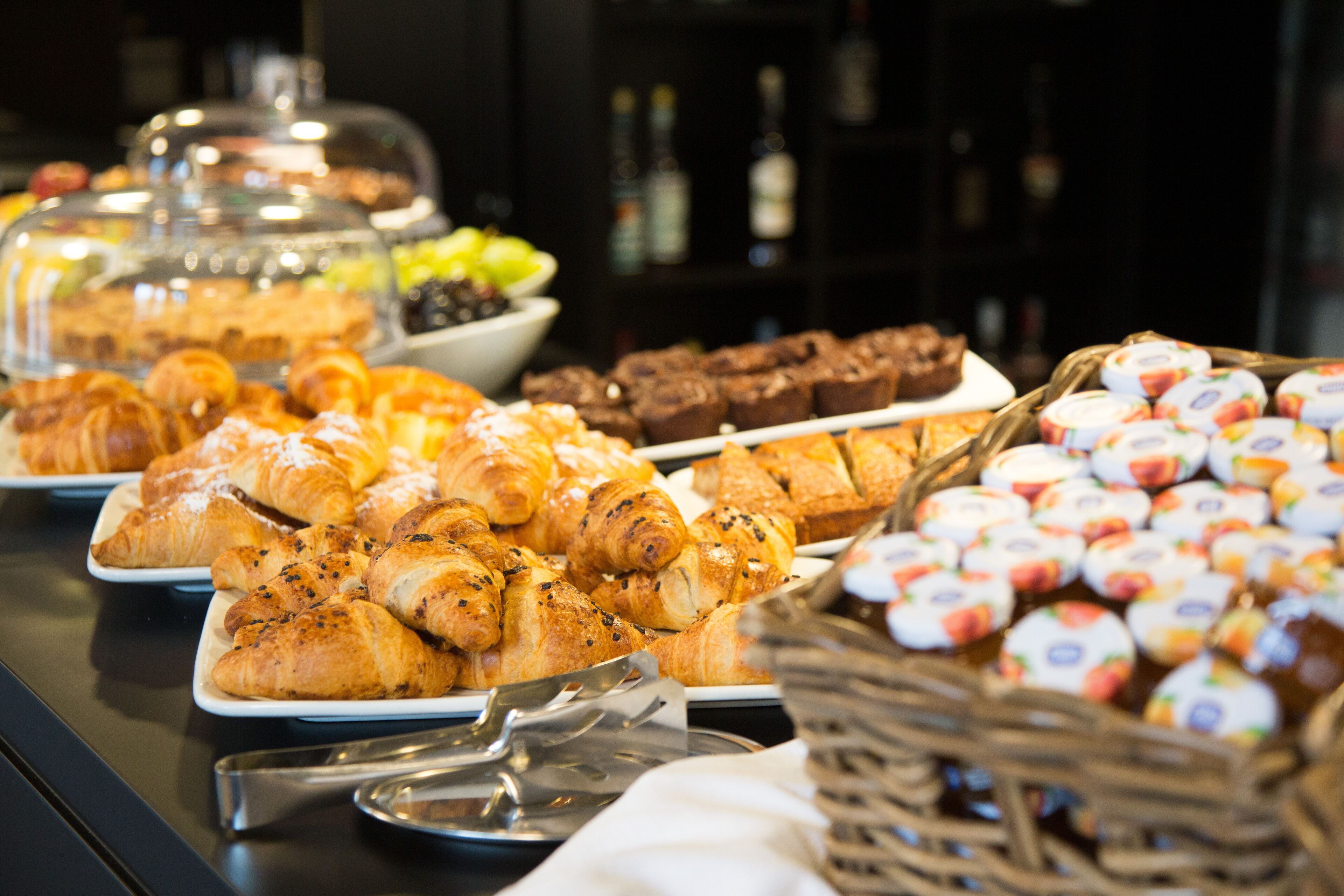 A buffet with various pastries and desserts, including croissants and brownies, arranged on plates and in baskets.