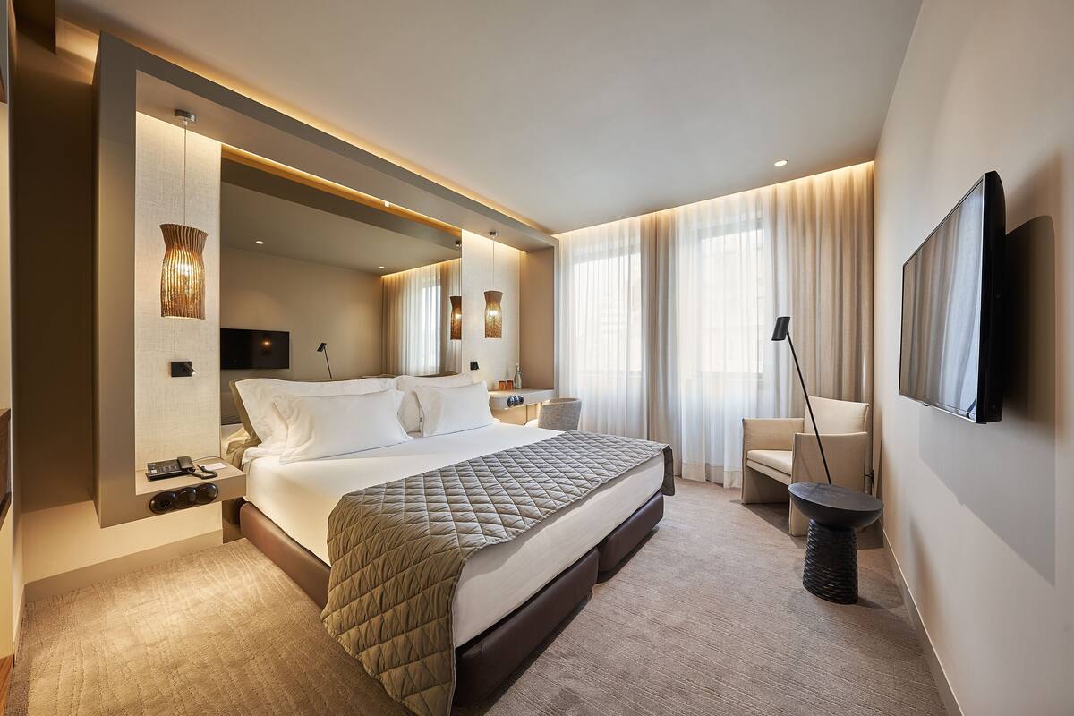 A modern hotel room with a large bed, bedside tables, a flat-screen TV, a desk, and a chair.