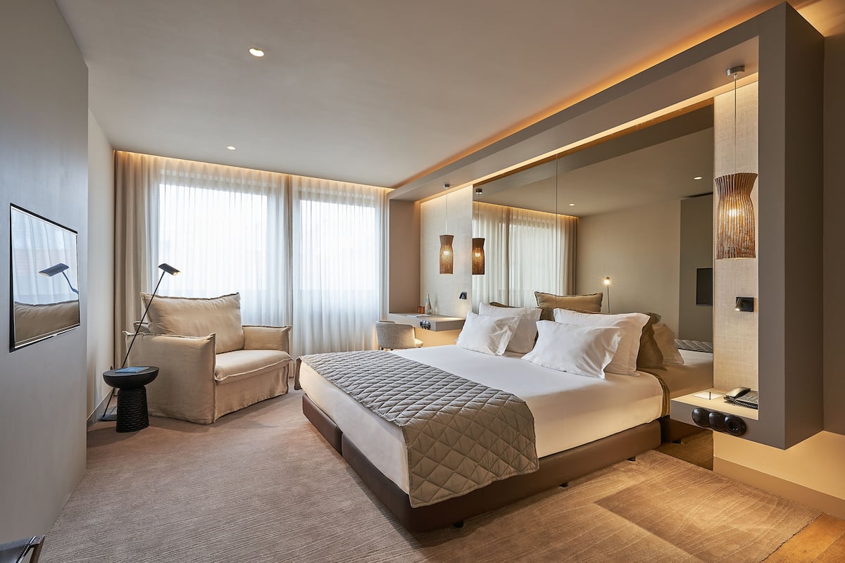 A modern hotel room with a large bed, a sitting area, and a large mirror.