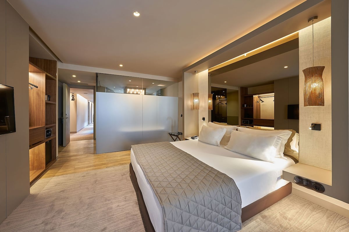 A modern hotel room with a large bed, a walk-in closet, and a bathroom with a large mirror.