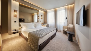 A modern hotel room with a large bed, bedside tables, a flat-screen TV, and a seating area with a chair and a small table. - PortoBay Teatro (Porto)