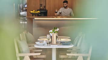 A restaurant with a wooden interior, a counter with a person behind it, and a table set with plates, glasses, and a vase with flowers.