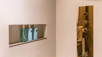 A bathroom with a shelf holding three bottles of liquid, a gold-colored shower panel, and a faucet.