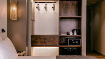 Una habitación de hotel moderna con cama, cafetera integrada, microondas y refrigerador pequeño.