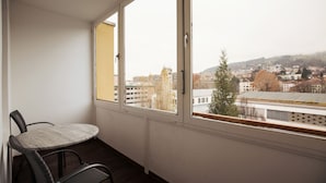 A balcony with a table and chairs, overlooking a cityscape with buildings and a hill. - Basic Hotel Innsbruck (Innsbruck)