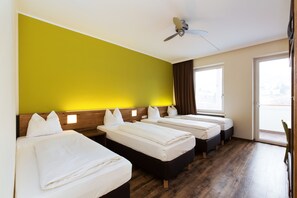 A hotel room with three beds, wooden flooring, a ceiling fan, and a large window. - Basic Hotel Innsbruck (Innsbruck)