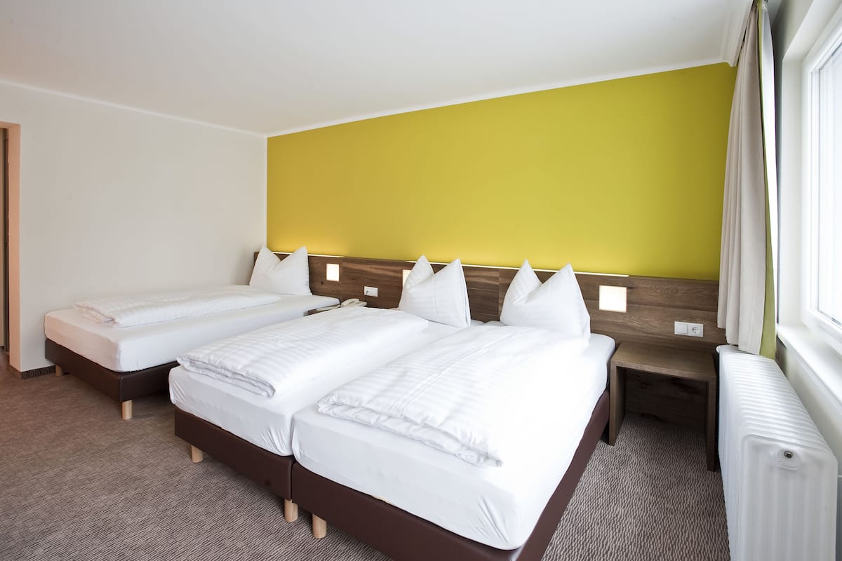 Una habitación de hotel con dos camas individuales, cabecera de madera, una mesita de noche pequeña y una ventana con cortinas.