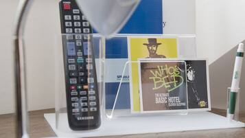 Un escritorio con una lámpara de escritorio blanca, un control remoto de Samsung y un atril con libros y un póster.