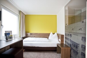 Quarto de hotel com cama, escrivaninha e janela com cortinas.