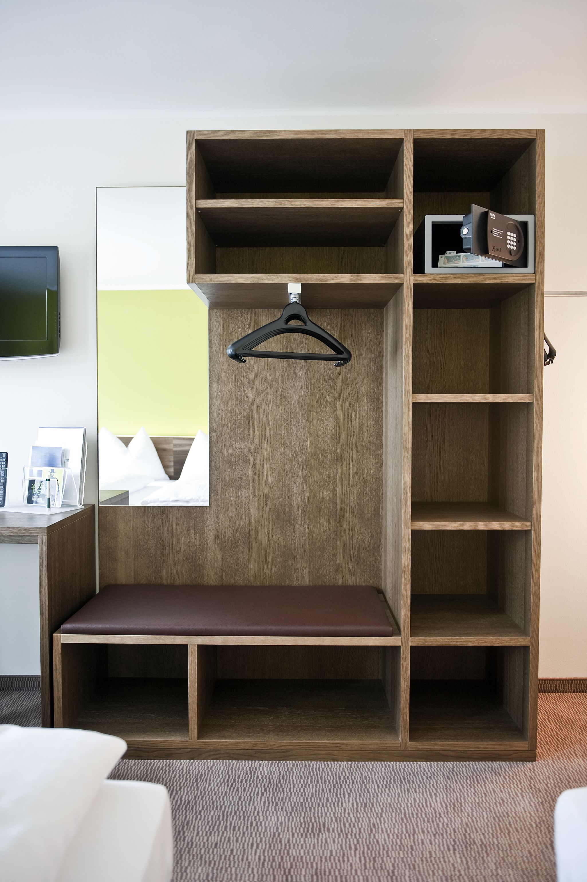 Habitación de hotel con armario de madera, un banco y perchero.