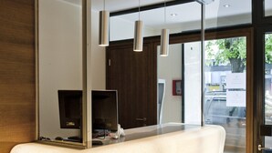 A reception desk with a large mirror, a flat-screen TV, and pendant lighting. - Basic Hotel Innsbruck (Innsbruck)